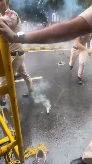 Still from the clip: a uniformed officer beside a barricade, with a gas canister smoking on the ground.