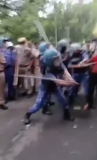 An officer swinging a lathi at women protesters